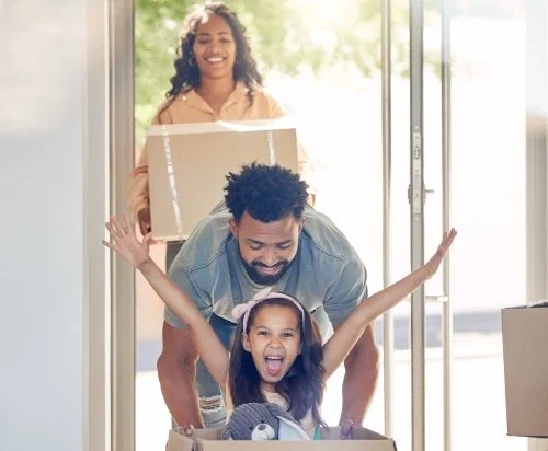 playful girl riding in a moving box with her cheerful family in San Diego, California